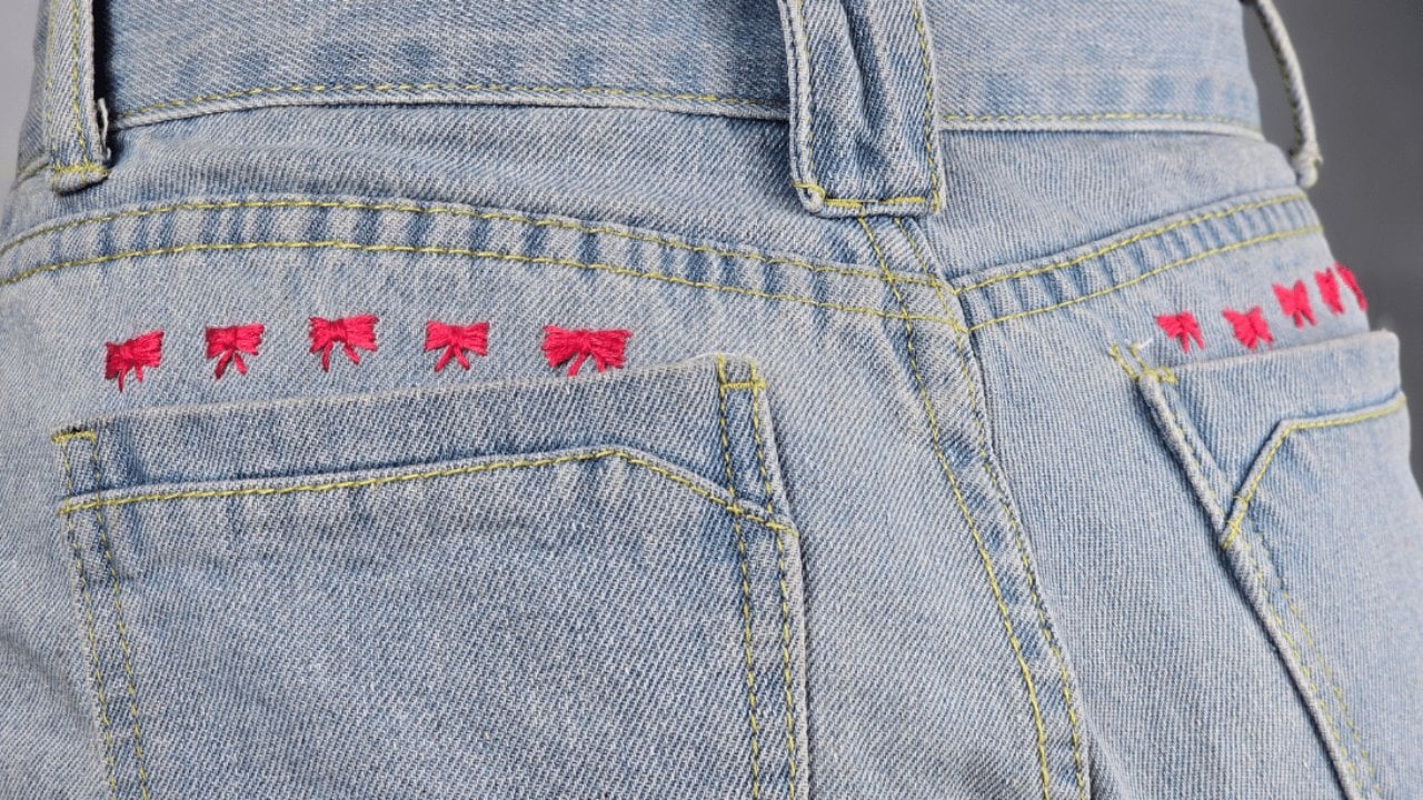 Pale blue jeans with a neat row of small red embroidered bows stitched along the back yoke above the pockets