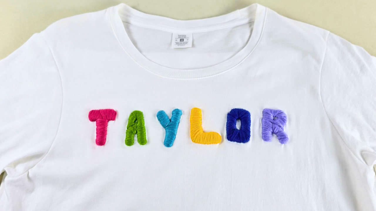 The name Taylor embroidered on a plain white t shirt in raised multicolored letters over a hot glue outline