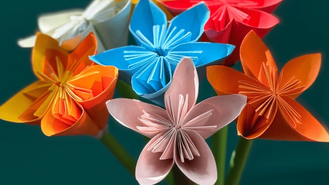 Origami Daffodils Easy Paper Flower Tutorial Origami paper flowers in orange, blue, coral and pale pink with folded petals, arranged as a bouquet on dark teal