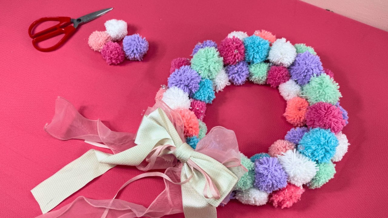 Easy DIY Pom Pom Wreath, Yarn pom poms wound around two bits of cardboard, then glued shoulder to shoulder around a wreath