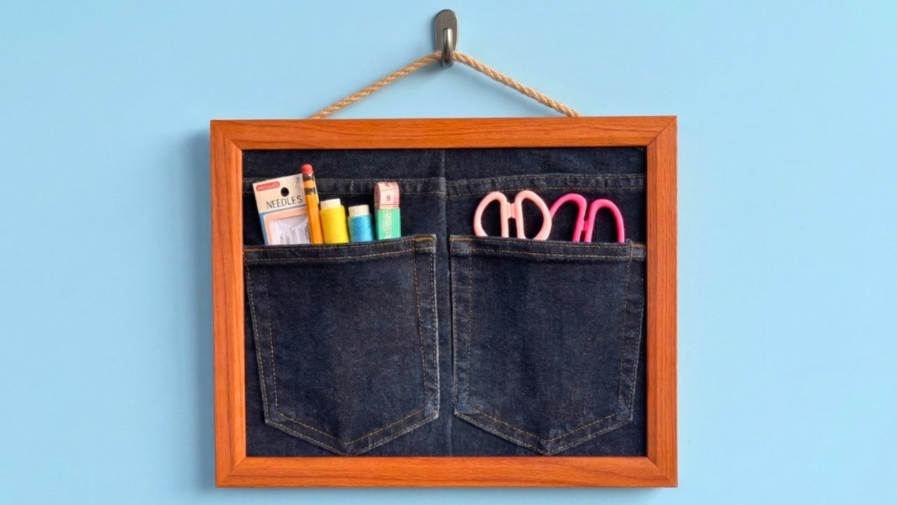 Wall organizer made from the back of a pair of jeans stretched in a picture frame, pockets holding craft tools
