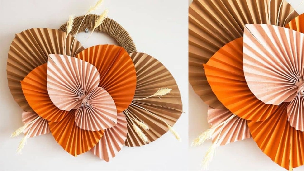 Pleated paper palm leaves in rust, orange and blush arranged as boho wall decor with dried grasses tucked between