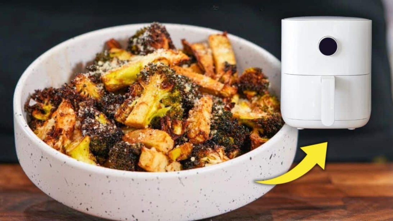 Charred air fryer parmesan crusted broccoli heaped in a speckled white bowl, tips blackened and dusted with parmesan