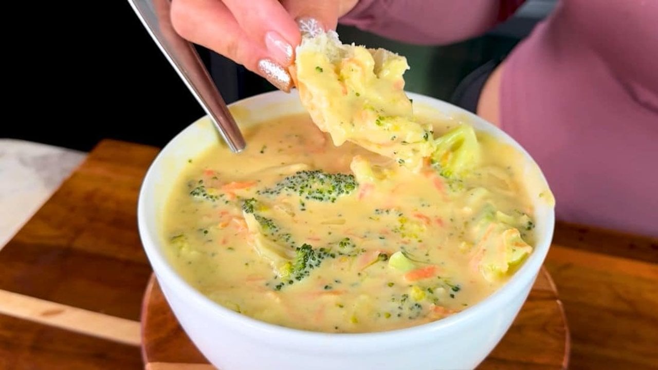 Copycat Panera broccoli cheddar soup in a white bowl with broccoli and carrot, bread being dipped in