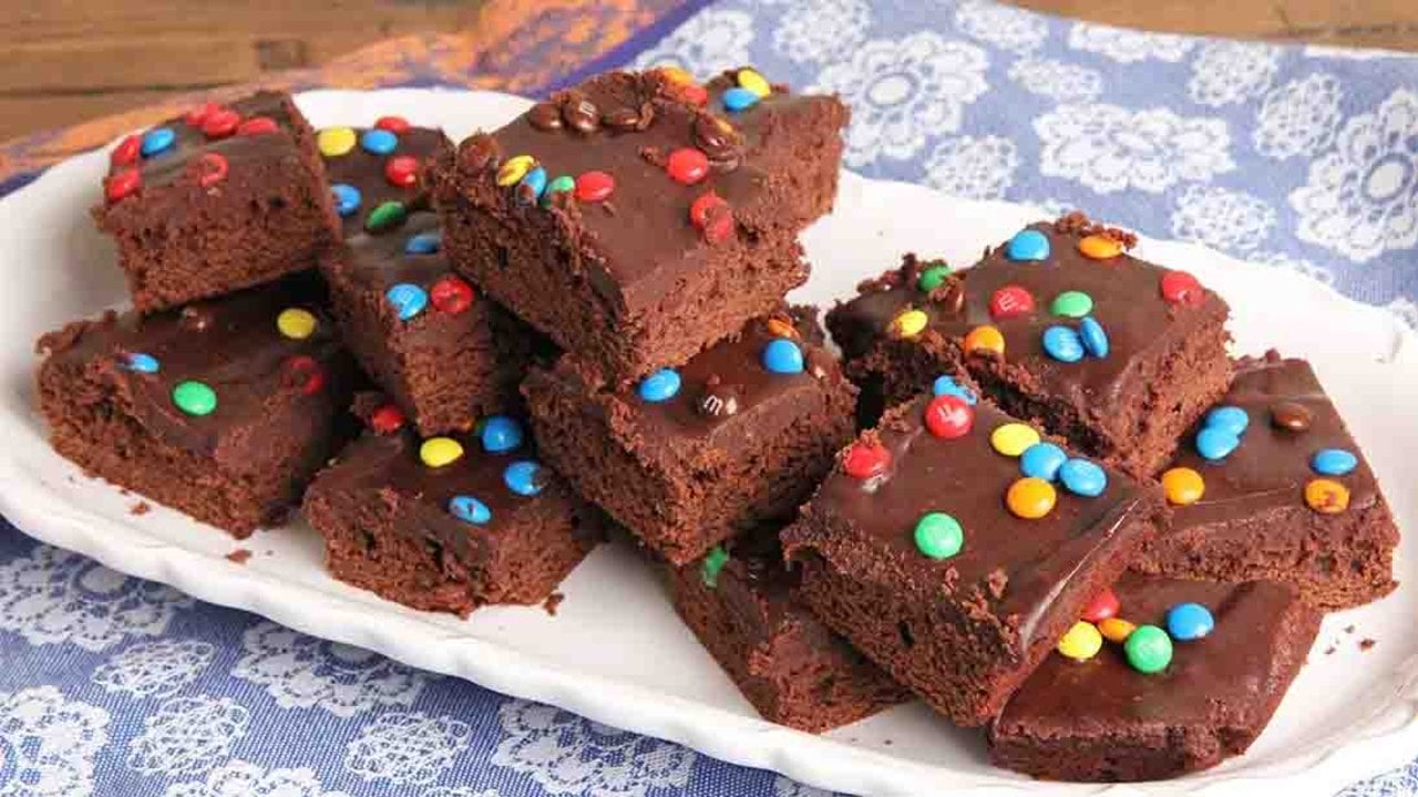Homemade Cosmic Brownies Recipe Homemade cosmic brownies cut into squares under chocolate ganache and mini candies on a white serving platter
