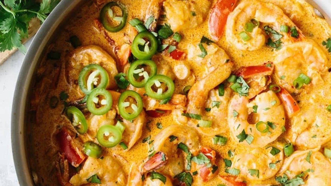 Creamy chipotle shrimp in a skillet with red pepper, chopped cilantro and sliced jalapeno in a smoky sauce