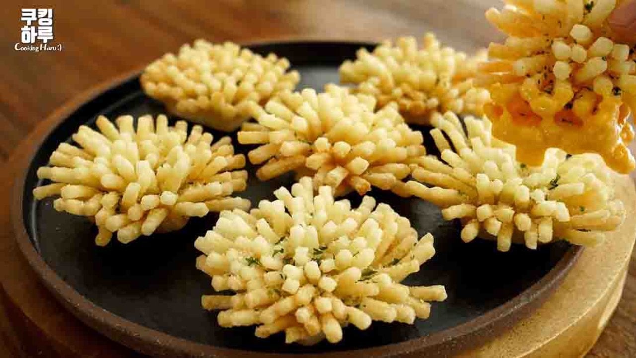 Crispy Fried Potato Flowers Recipe Deep fried potato flowers with spiky golden petals on a black plate, one being lifted with cheese dip