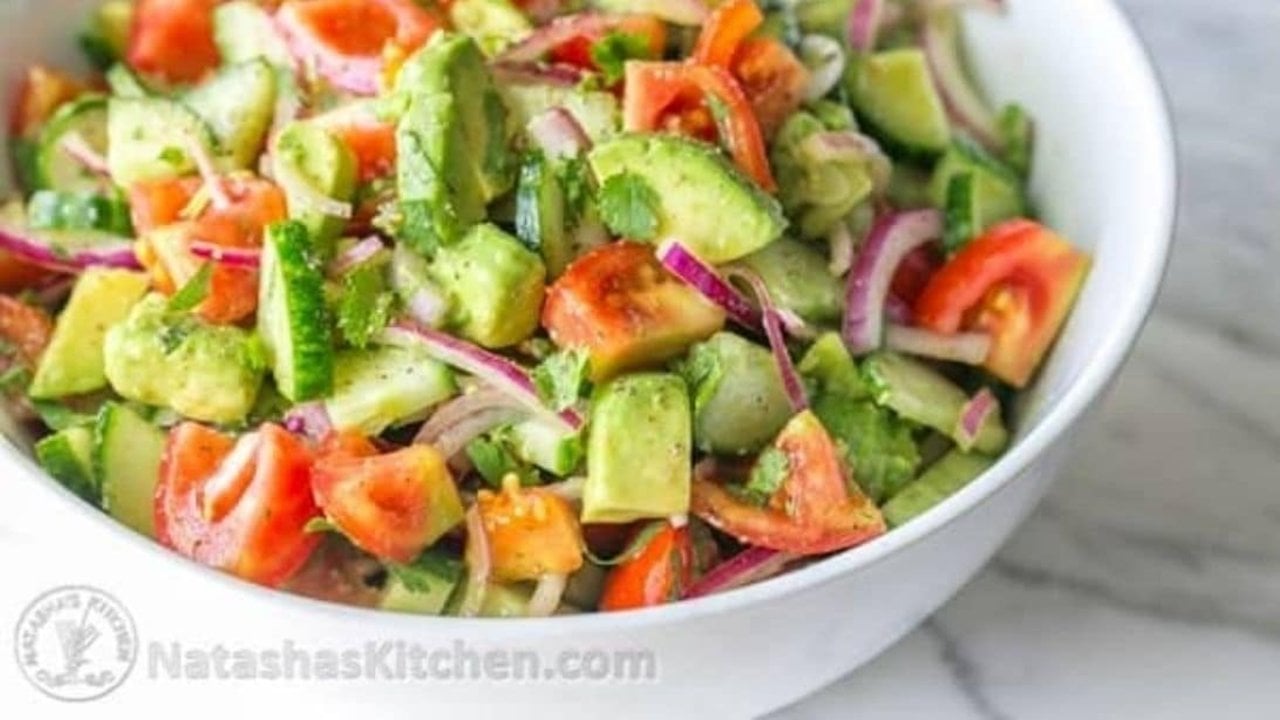 Cucumber Tomato And Avocado Salad White bowl of cucumber tomato and avocado salad on marble, sliced red onion and chopped herbs, shot from above