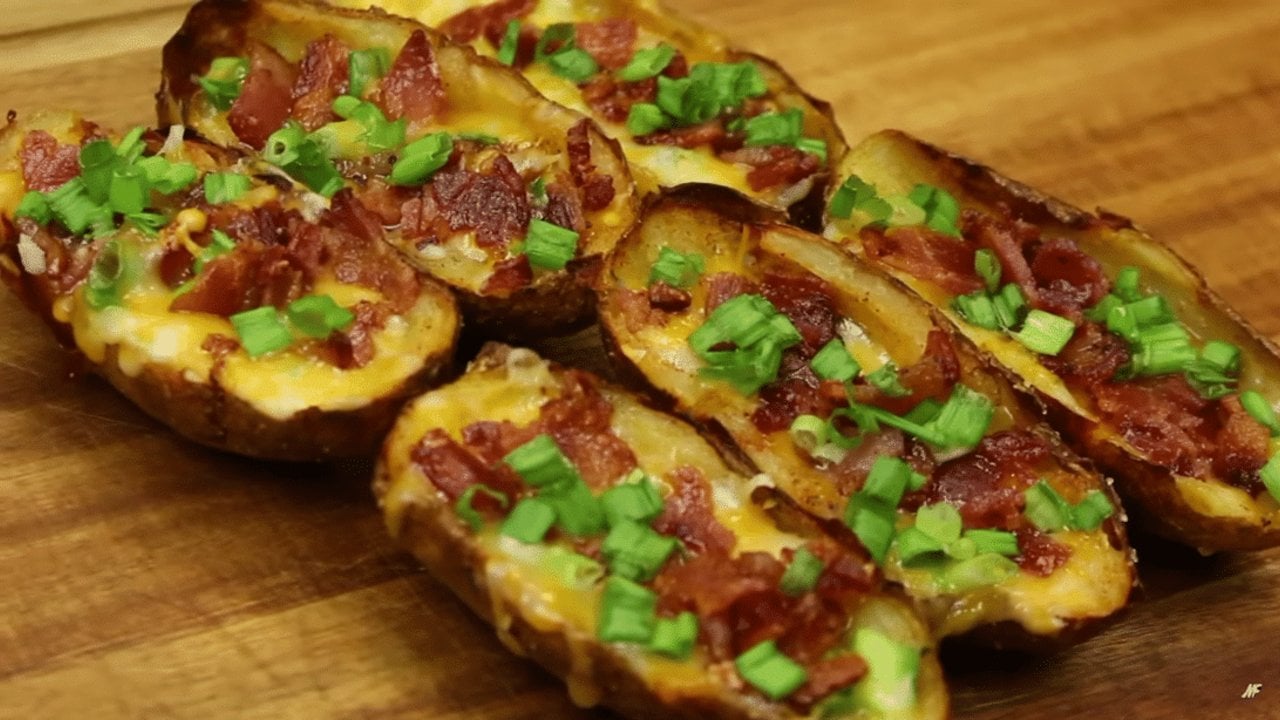 Easy Baked Potato Skins Side Dish Baked potato skins filled with melted cheese, crisp bacon and chopped green onion on a wooden serving board