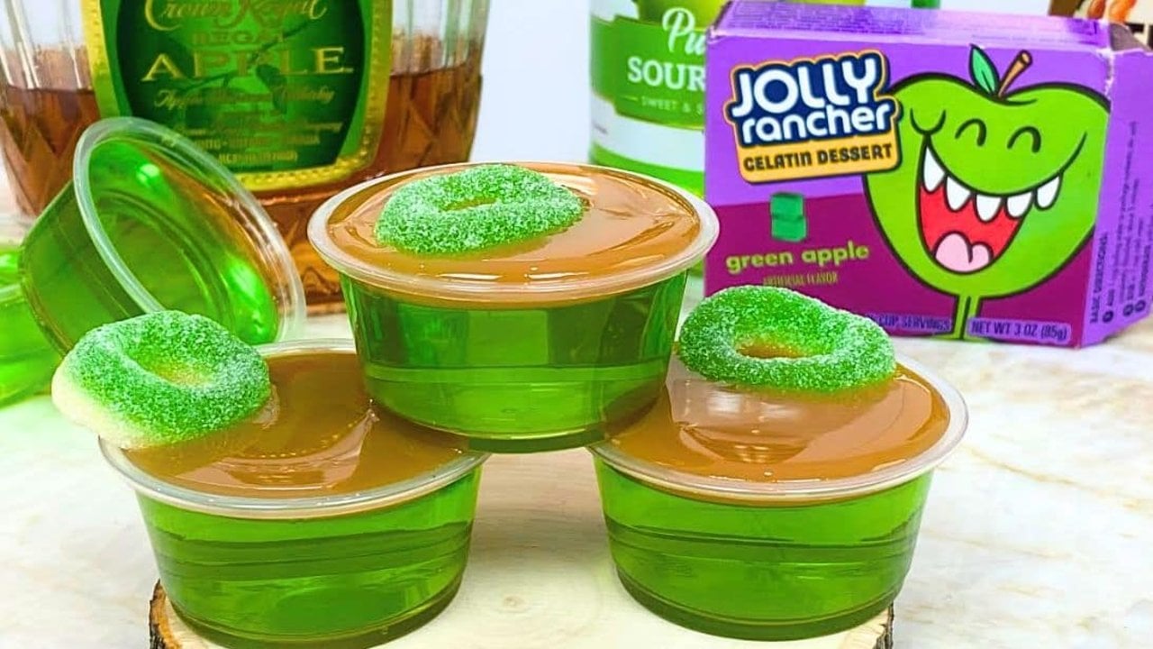 Crown caramel apple jello shots in small cups topped with caramel sauce and a green apple ring candy