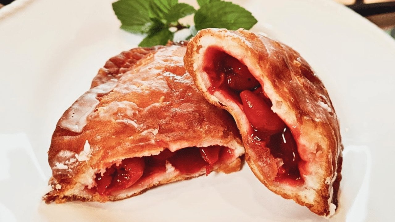 Fried cherry pies made with canned biscuits, sealed with a fork and drizzled with powdered sugar glaze