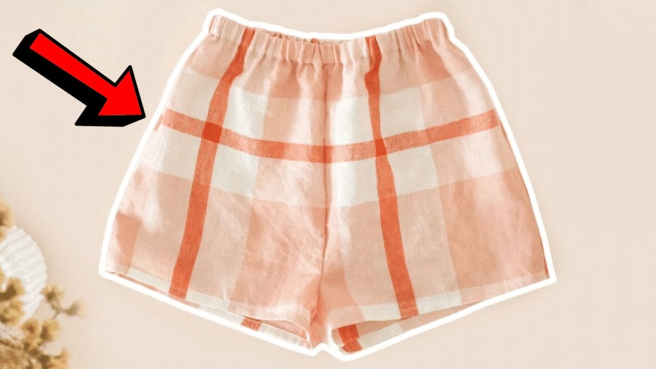 Pink and white checked pajama shorts with an elastic waist laid flat, with a large red arrow pointing at them