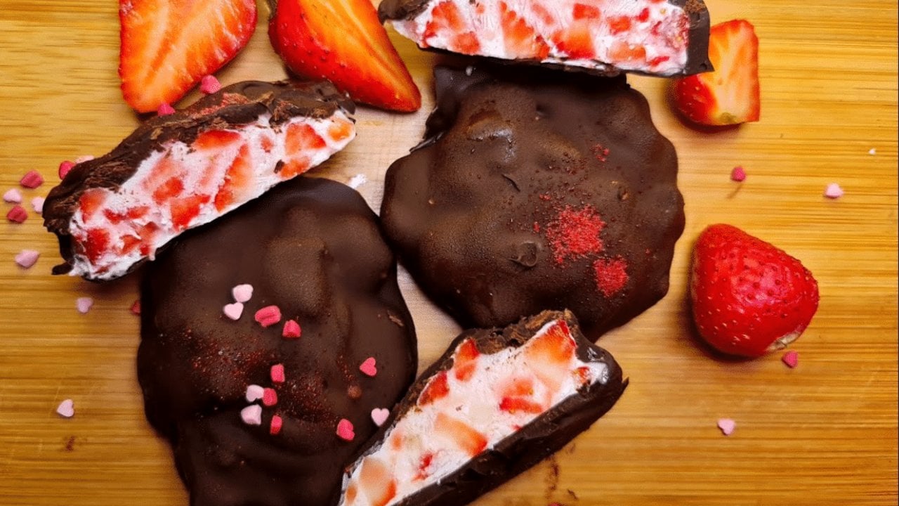 Frozen strawberry yogurt clusters dipped in dark chocolate with pink heart sprinkles on a wooden board