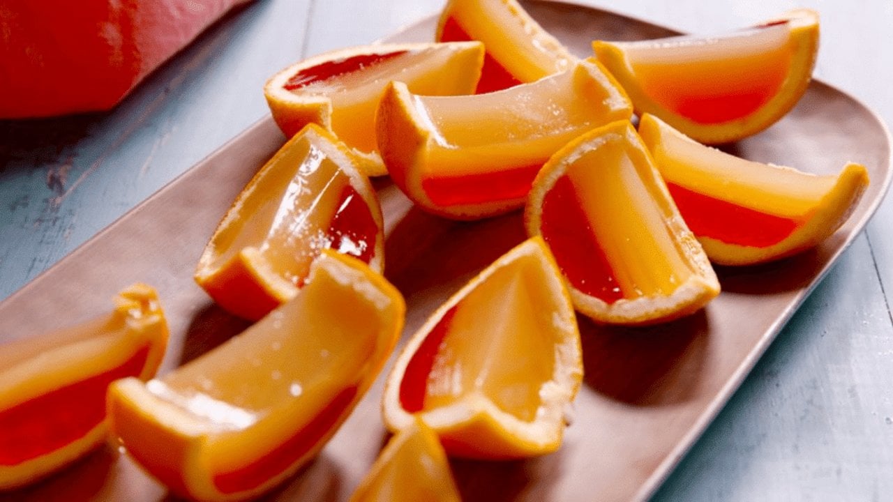 Tequila sunrise jello shots set inside hollowed orange halves and cut into wedges showing the red layer