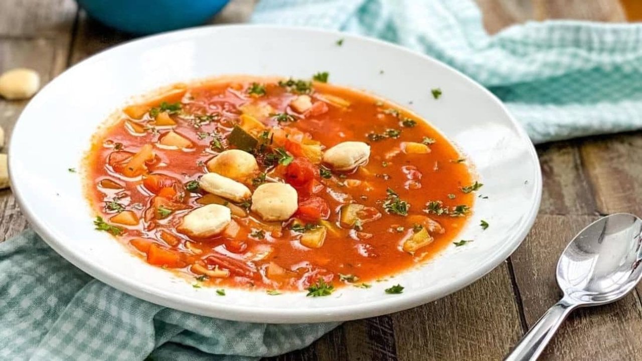 Manhattan clam chowder in a white bowl, red tomato broth with diced vegetables and oyster crackers on top