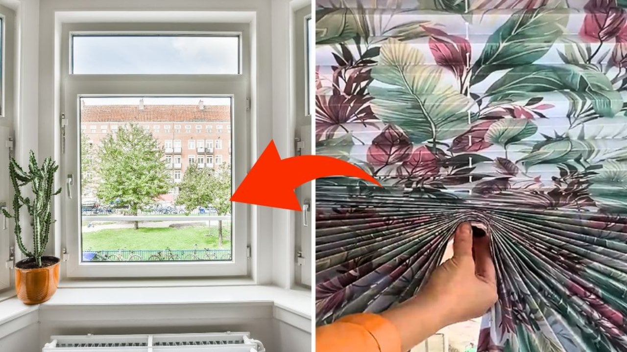 DIY blinds using wallpaper, a hand fanning open a pleated leaf print paper blind beside a bright window with a cactus