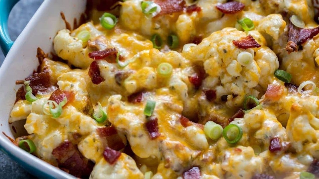 Loaded Cauliflower Casserole Keto Side Loaded cauliflower casserole under melted cheddar with bacon and green onion in a white dish with a blue rim