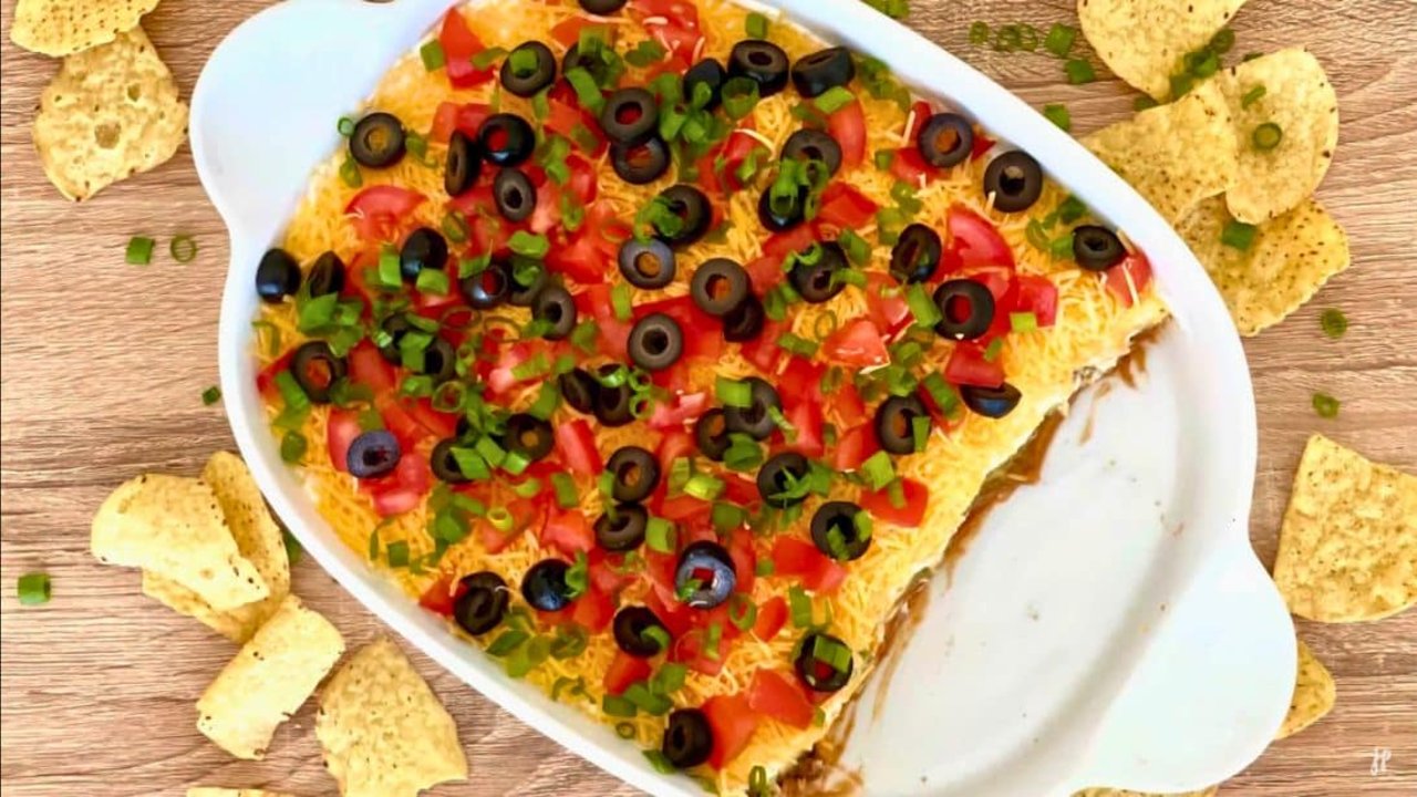 Mexican 7 Layer Party Dip Recipe Mexican 7 layer party dip in a glass dish with refried beans, guacamole, sour cream, cheese and black olives