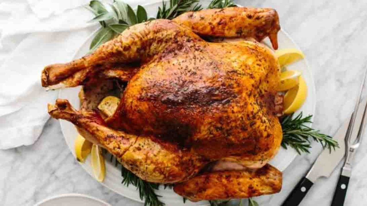 No-fail roast Thanksgiving turkey with golden brown skin resting on a platter with fresh herbs and lemon