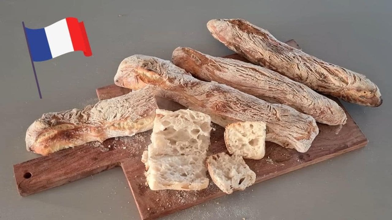 No knead baguettes with crisp slashed crusts cooling on a rack after baking, dusted with a little flour
