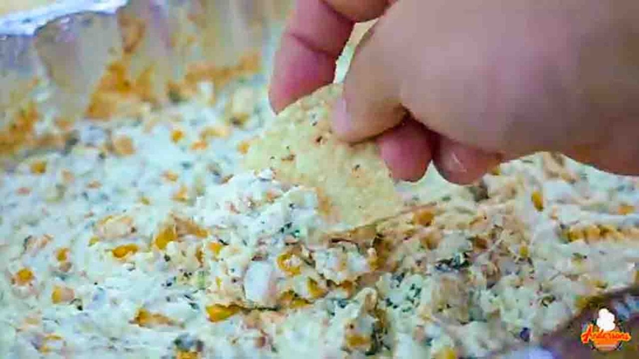 Smoked street corn dip in a cast iron skillet with cotija, cilantro and Tajin over melted cheese on a cookout table