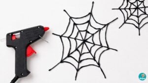 Halloween Crafts - a black glue gun and two finished black hot glue spider webs laid out on a white background