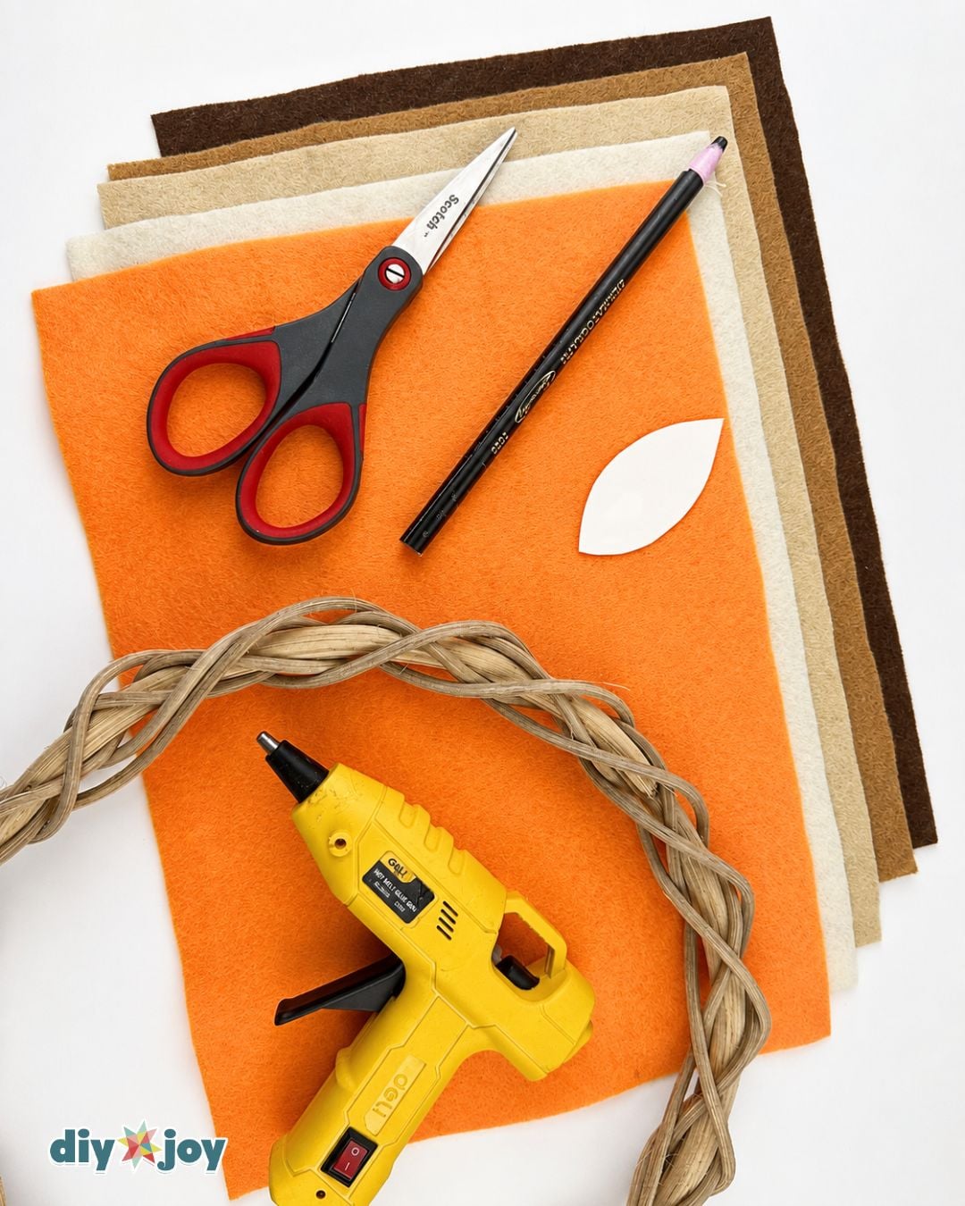 Fall wreath supplies - felt sheets, scissors, pencil, leaf pattern, glue gun, and a grapevine wreath