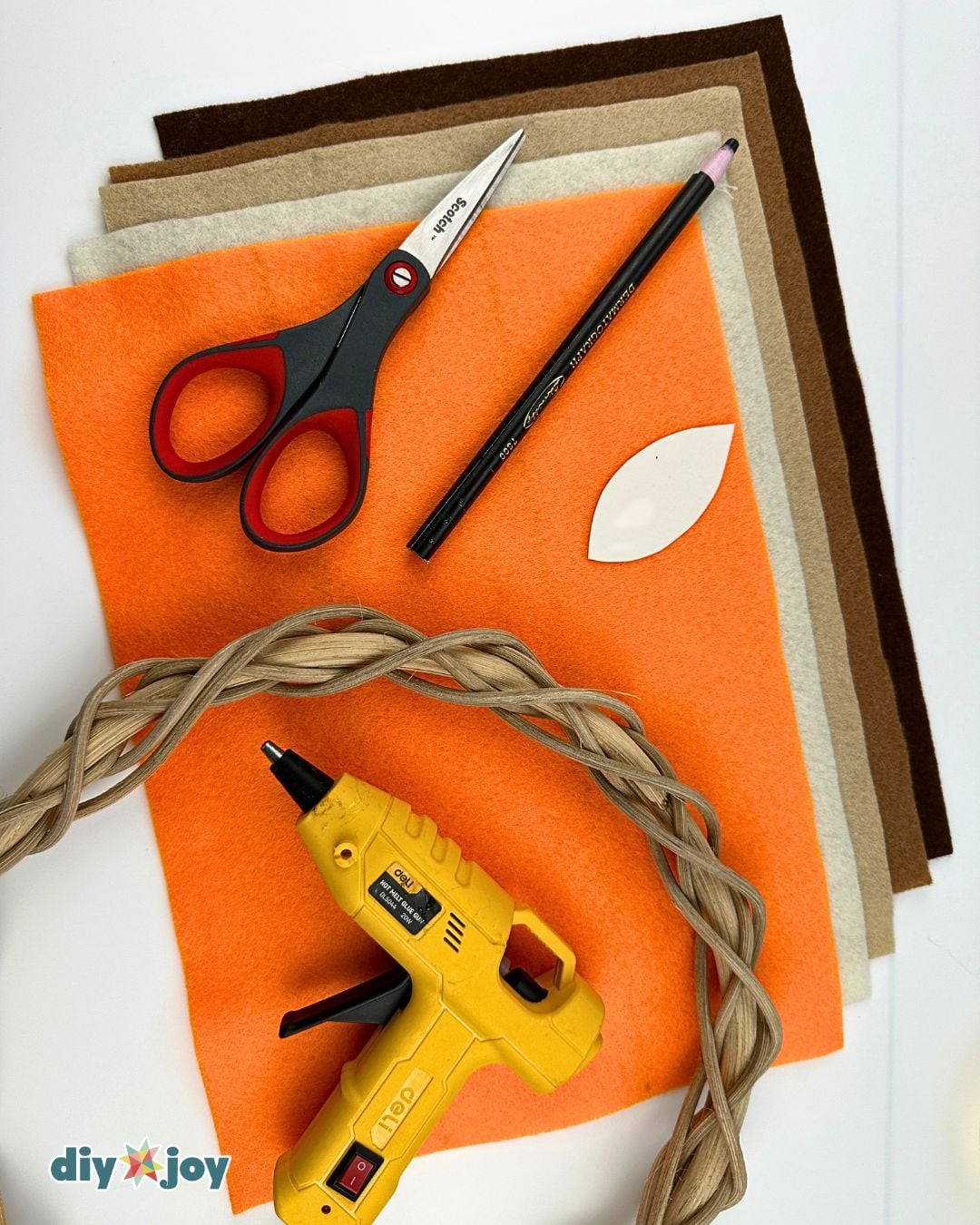 Fall wreath supplies - felt sheets, scissors, pencil, leaf pattern, glue gun, and a grapevine wreath