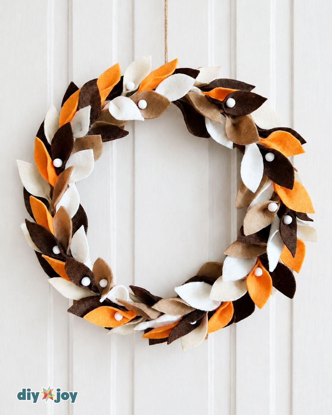 Easy DIY fall wreath tutorial - finished felt leaf wreath with white pom-poms hanging on a door