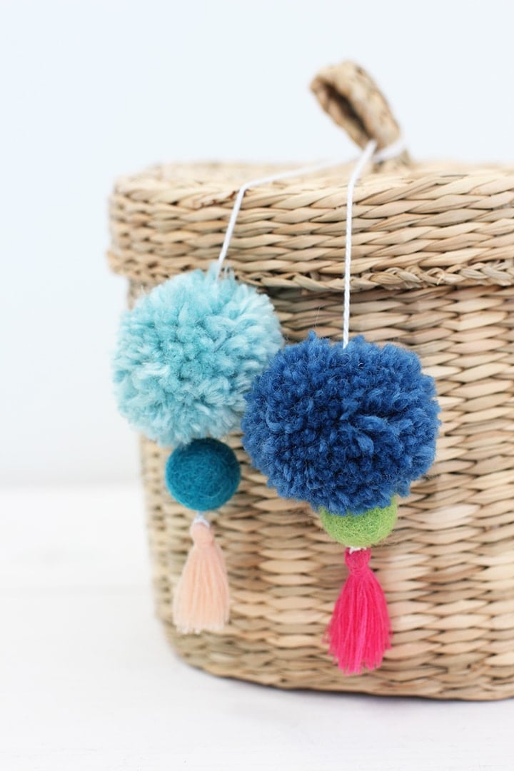 DIY pom tassel storage basket, a handmade Mom gift decorated with yarn pom poms and mini thread tassels tied to the lid.