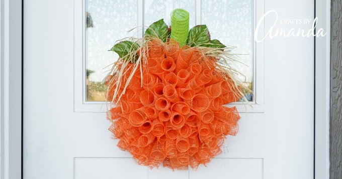 Orange deco mesh pumpkin wreath with a green stem hanging on a front door, a bright fall wreath for autumn