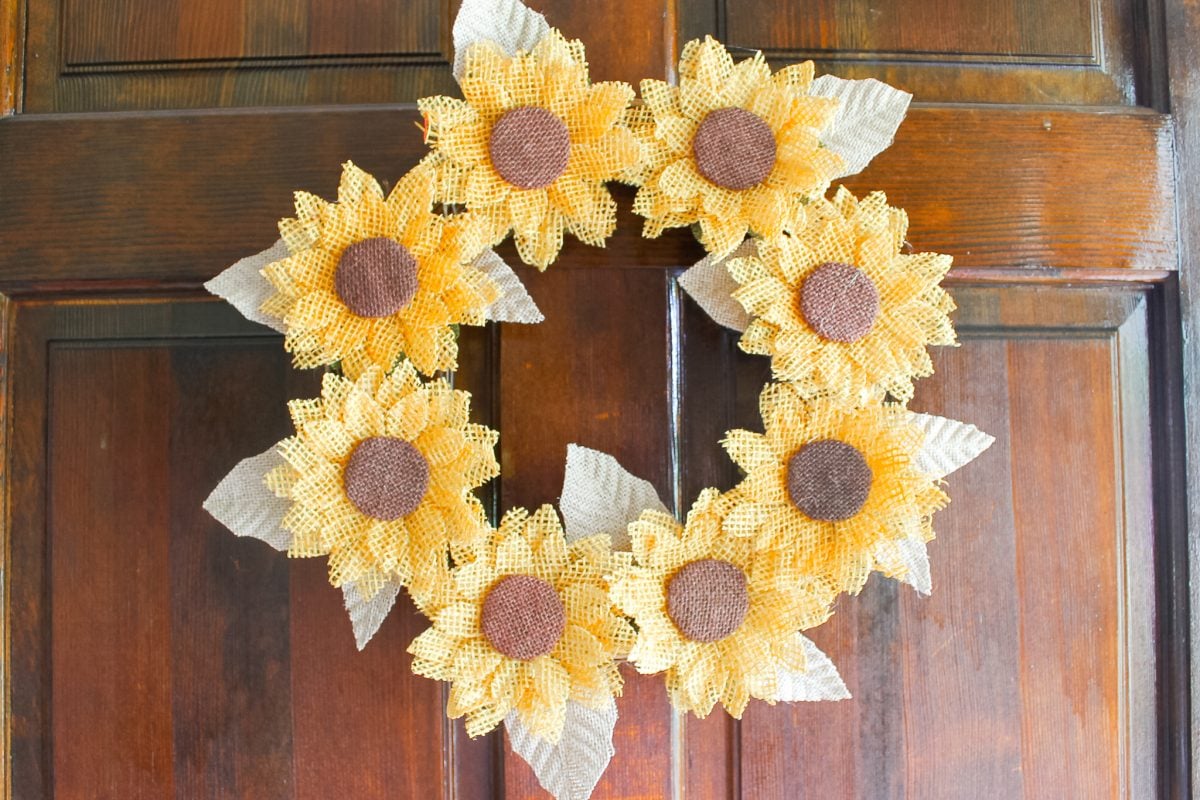 Burlap sunflower wreath with yellow burlap flower petals and fabric leaves hanging on a wood front door for fall