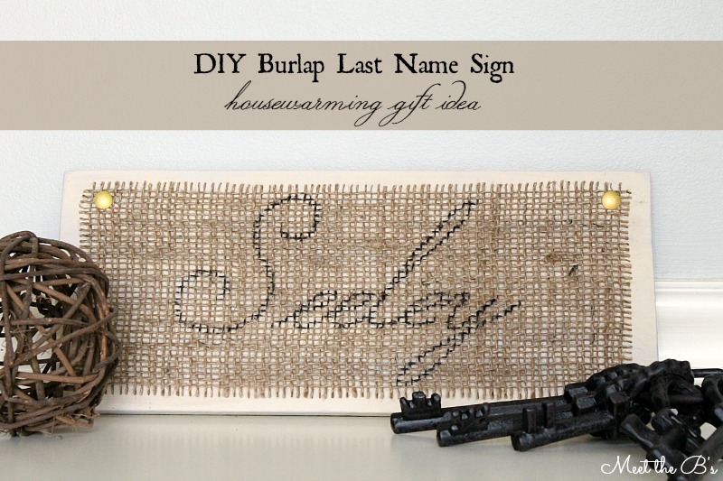 Cross stitched burlap last name sign with gold thumbtacks on painted wood, a DIY housewarming gift idea
