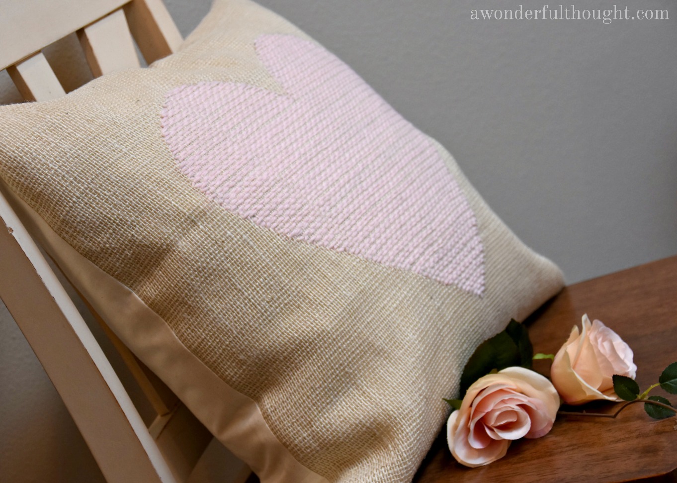 Burlap pillow with a woven pink heart design made by hand weaving yarn through the fabric squares