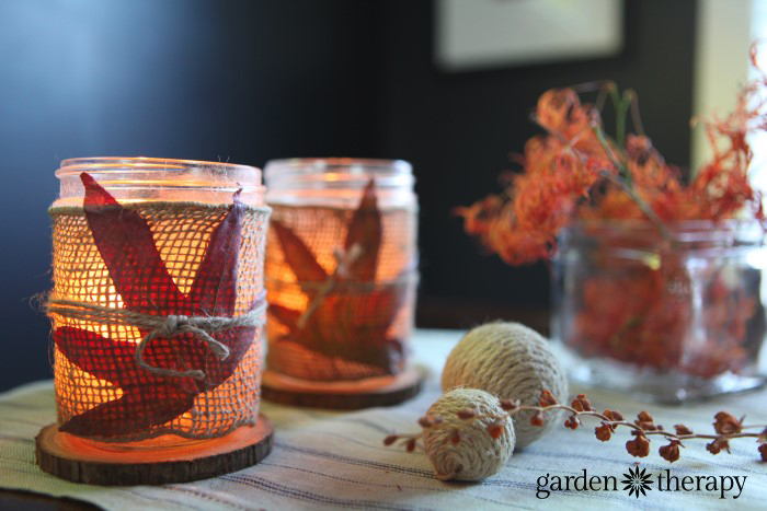 Burlap wrapped mason jar candle holders decorated with pressed fall leaves and lit with tea lights