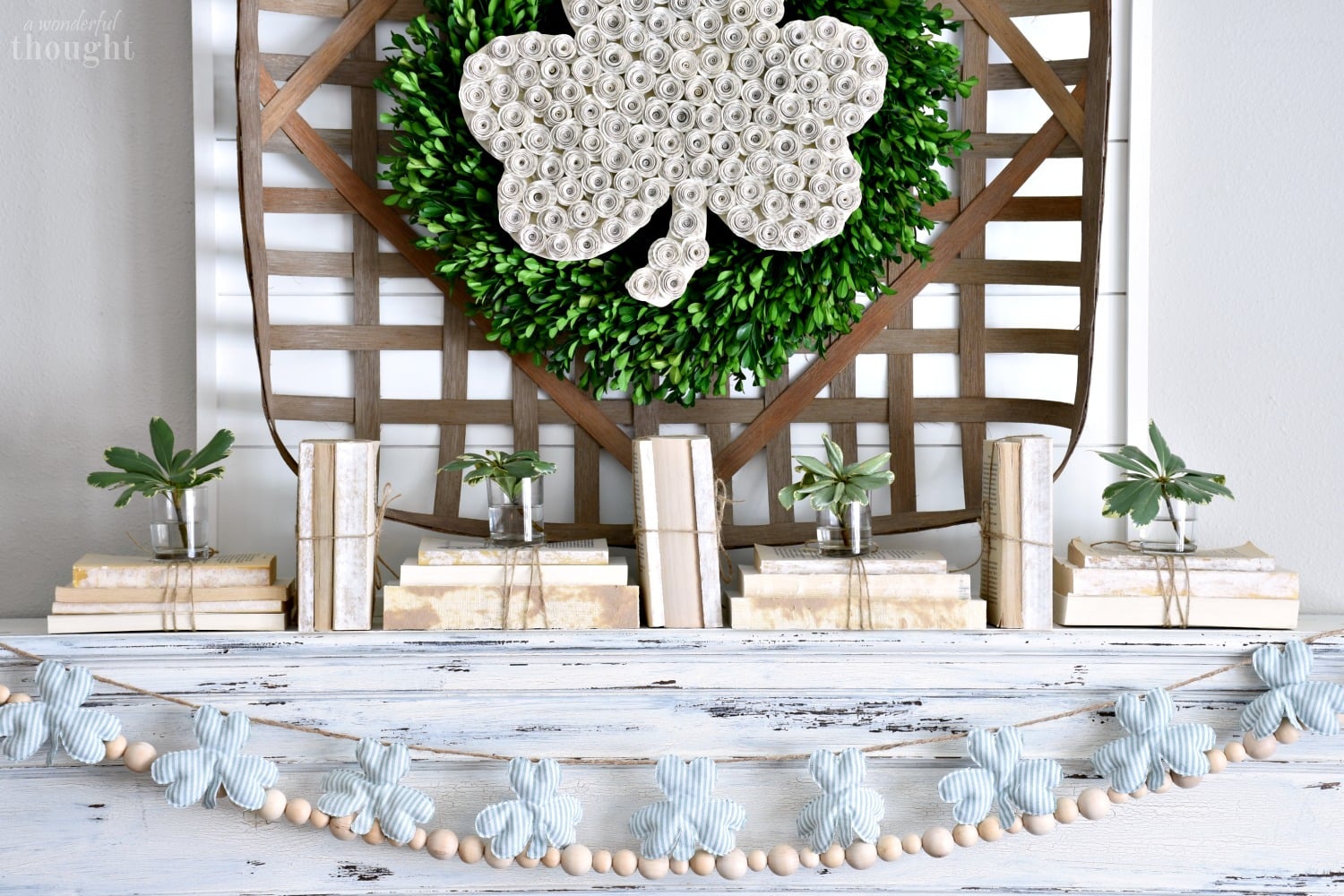 Boxwood wreath with a paper shamrock and fabric shamrock garland styled on a farmhouse mantel for St Patricks Day