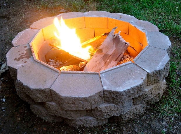 Circular brick fire pit burning in a gravel backyard seating area