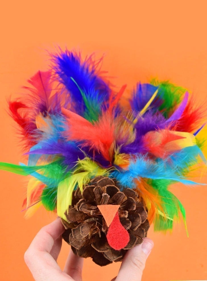 DIY pinecone turkey craft with colorful feathers and googly eyes, an easy fall activity for kids to make