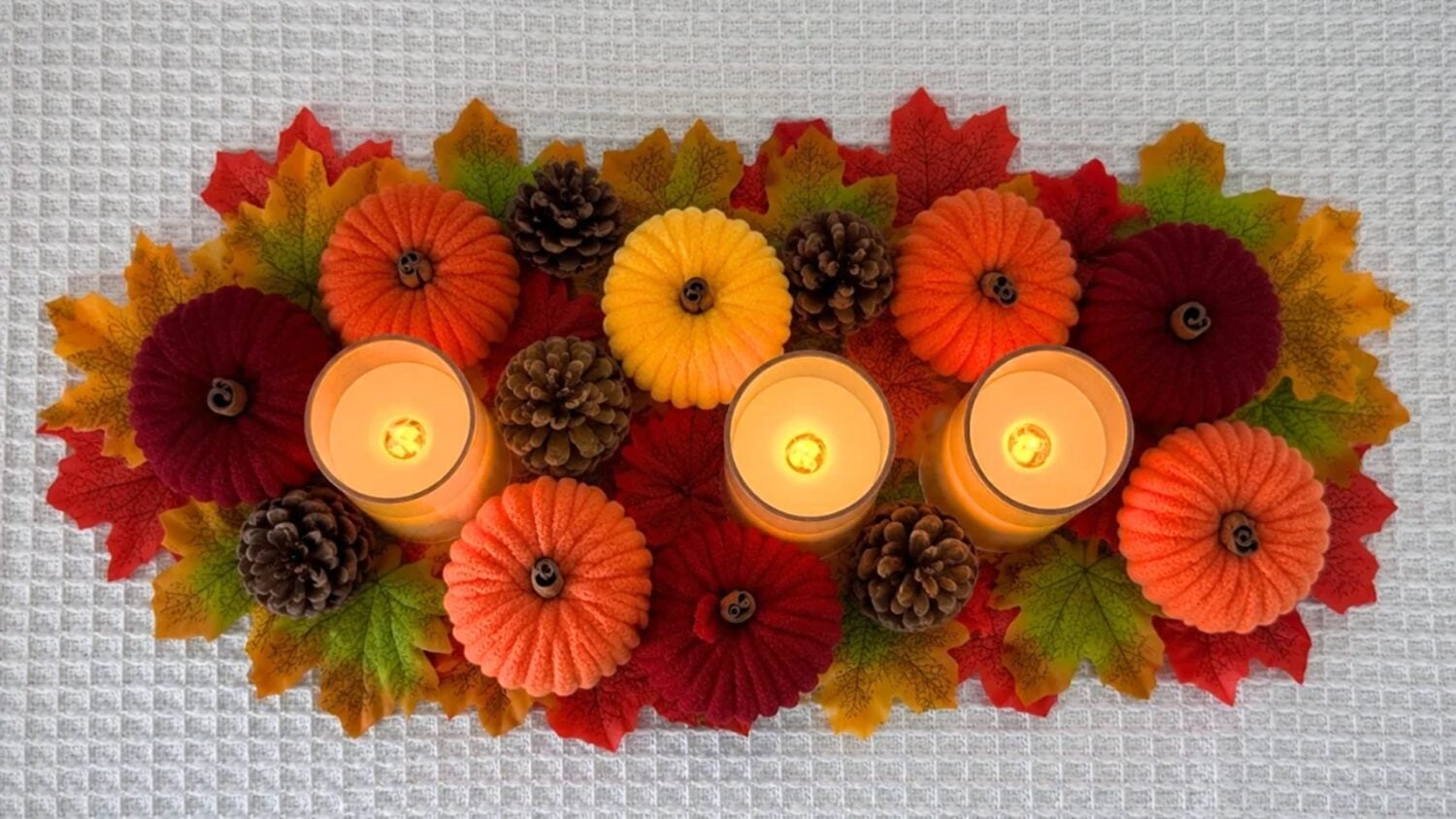 Fall Crafts - yarn wrapped toilet paper roll pumpkins arranged with faux autumn leaves, pinecones, and glowing tealights as a table centerpiece