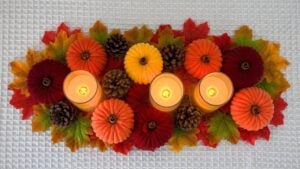 Fall Crafts - yarn wrapped toilet paper roll pumpkins arranged with faux autumn leaves, pinecones, and glowing tealights as a table centerpiece