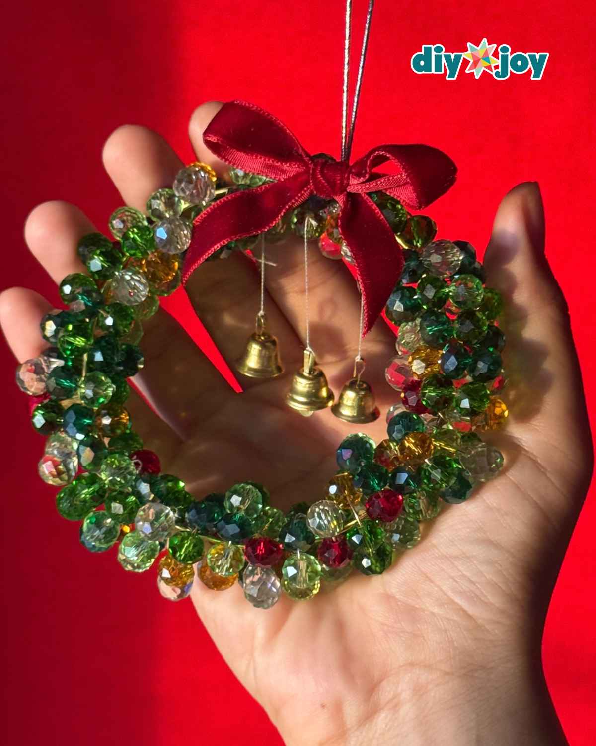 Hand holding a handmade Christmas wreath ornament covered in green, red, gold and clear faceted crystal beads