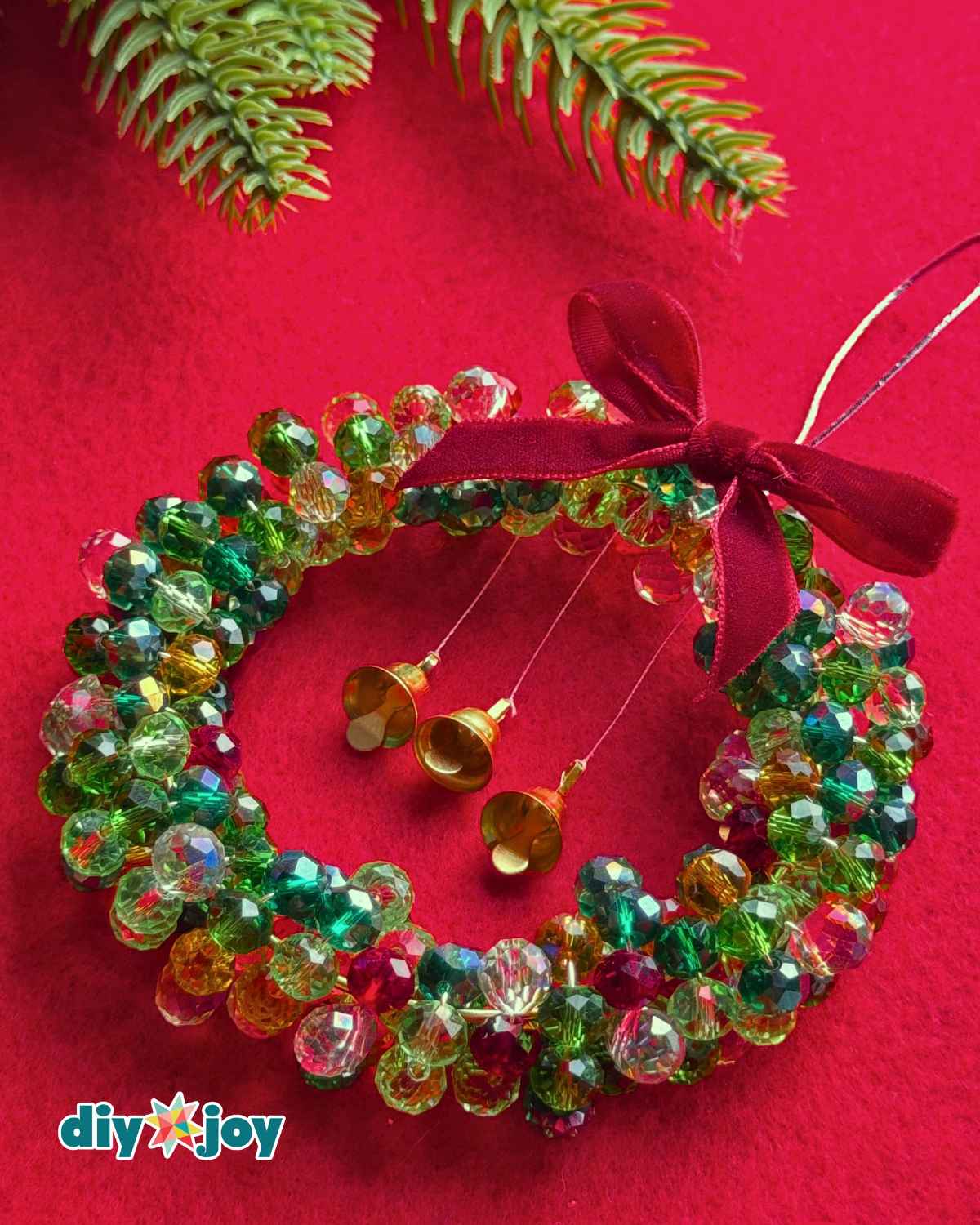 Crystal bead Christmas wreath ornament with a red bow and three miniature gold bells arranged on red felt