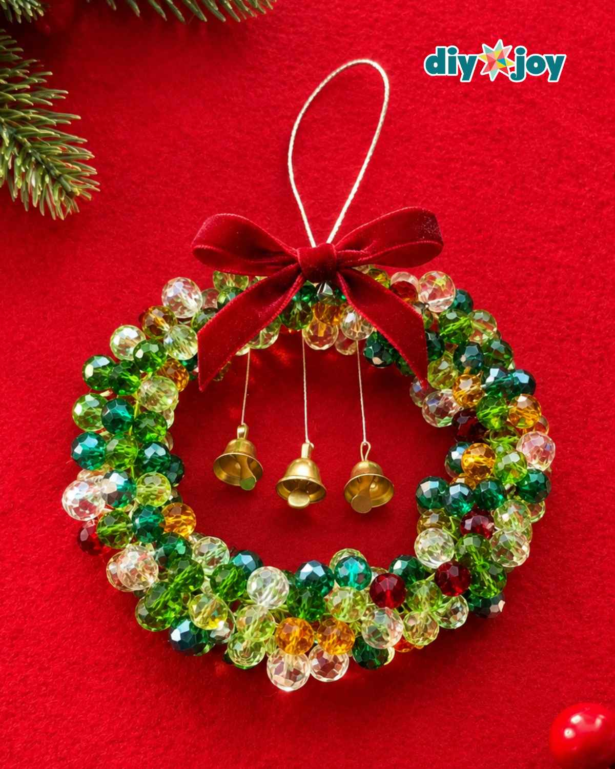 DIY beaded Christmas wreath ornament with a silver hanging loop, velvet bow and three bells on a red background