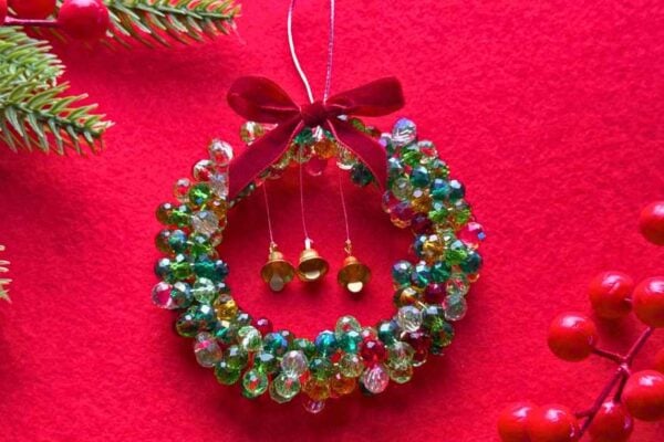 Beaded Christmas wreath ornament with green crystal beads, three gold bells and a red velvet bow on red felt