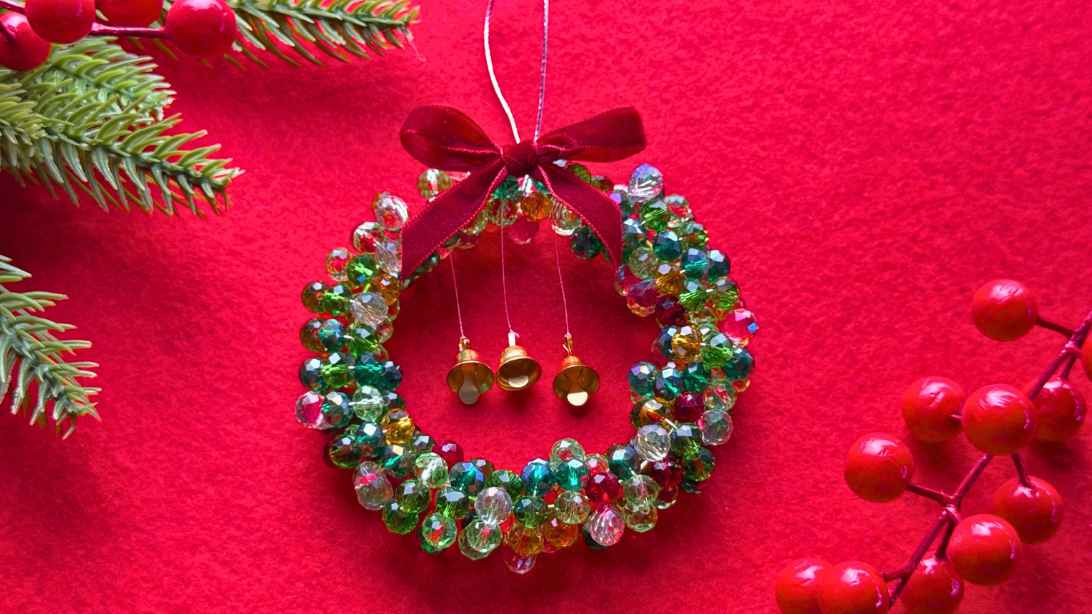 Beaded Christmas wreath ornament with green crystal beads, three gold bells and a red velvet bow on red felt