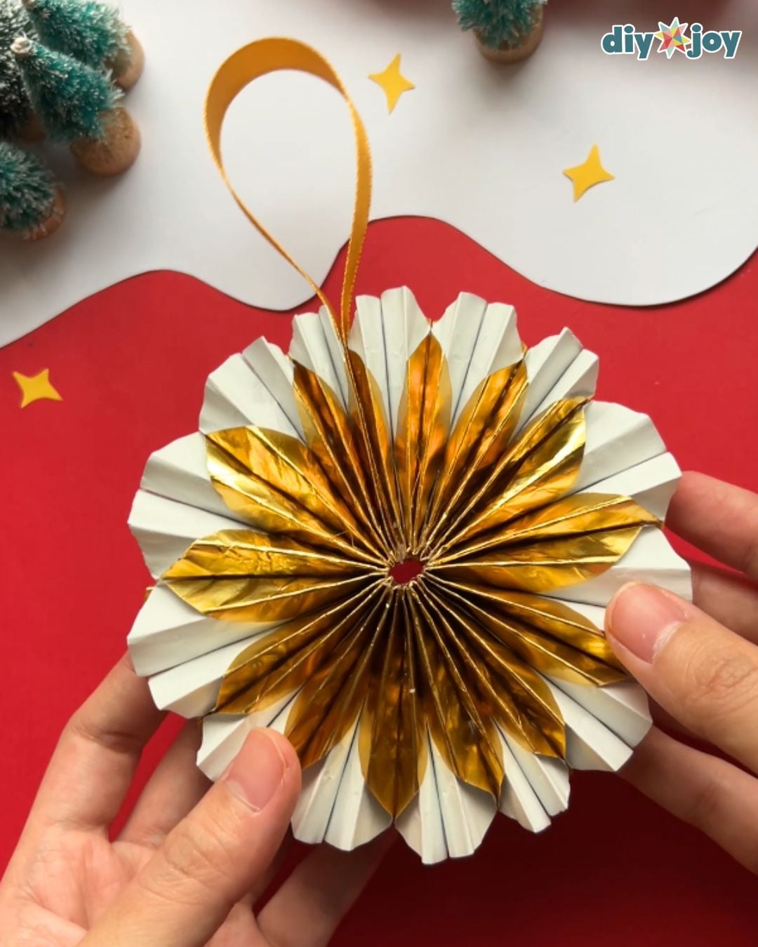 DIY Christmas Ornament | Finished Cupcake Liner Craft DIY Christmas ornament finished as a round gold and white paper fan with a ribbon loop, held in two hands