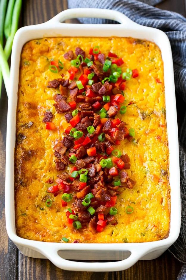 Loaded Corn Casserole Thanksgiving Side Corn casserole topped with bacon, cheddar, red peppers and green onions in a white handled baking dish