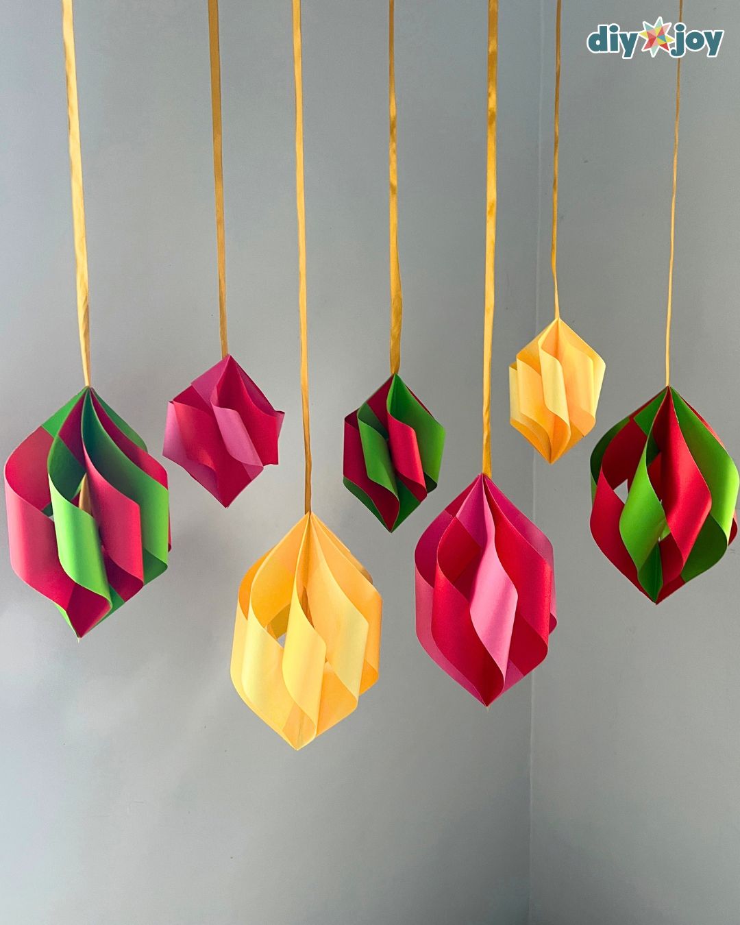A cluster of handmade paper ornaments dangles from gold ribbons in the corner of a room, cheerful DIY Christmas decor