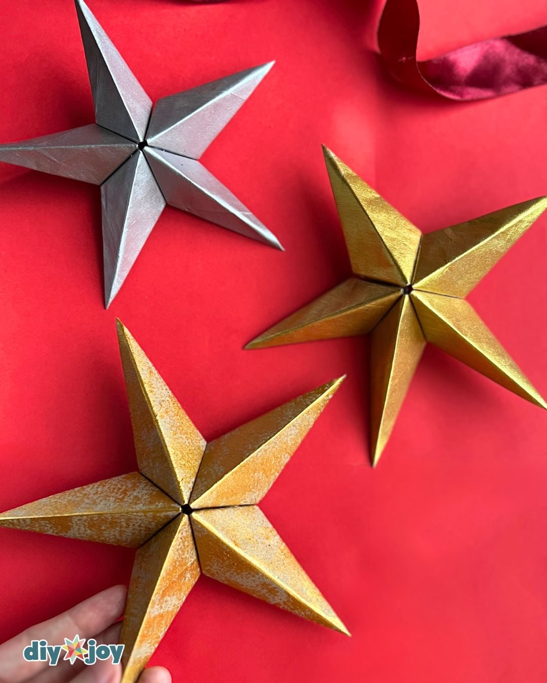 DIY paper star ornament - a silver and two gold 3D paper stars on a red background, homemade Christmas decor