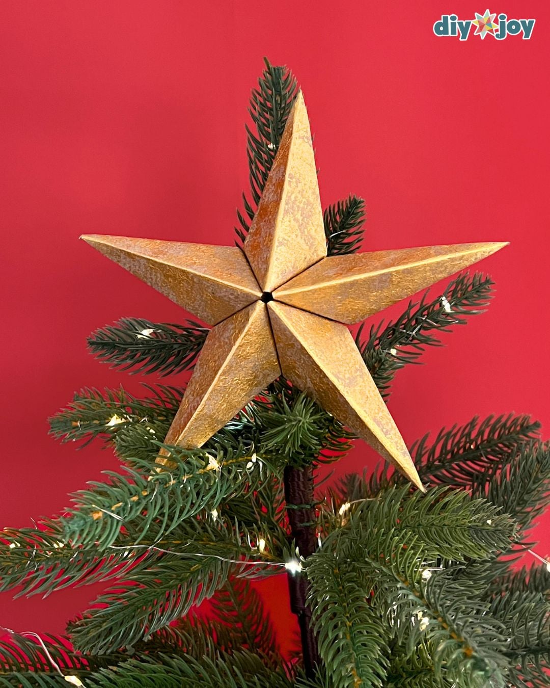 Paper bag star ornament as a tree topper, gold paper star nestled in pine with string lights at home